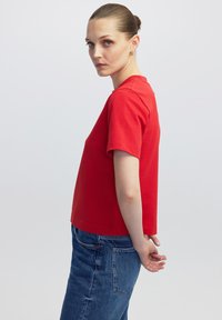 Červený krátký rukáv top s kulatým výstřihem a rovným zakončením, spárovaný se slim fit džíny středního praní. Hladká bavlněná tkanina.