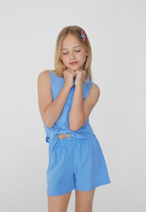 Chemisier sans manches bleu clair avec fermeture à boutons et devant noué, associé à un short assorti. Le tissu semble texturé et léger.