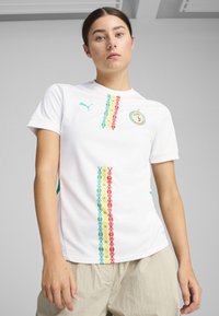 White short-sleeve sports shirt featuring colorful geometric patterns in green, red, and yellow. Puma logo on the left chest. Soft fabric.