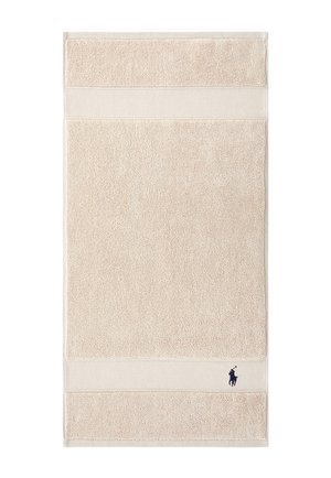 Beige cotton towel with textured bands near edges and a small dark blue embroidered polo player logo in the bottom right corner.