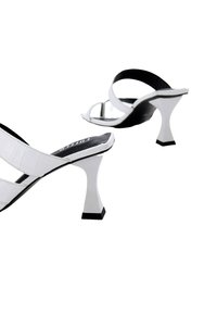 Witte hakken sandalen met zwarte accenten. Het strapdesign heeft een gestructureerde bovenkant en een onderscheidende geometrische hak.