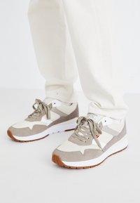 Sneakers beige e grigi con una combinazione di materiali in suede e mesh. Presentano una suola intermedia bianca e una suola in gomma gomma. Design classico con lacci.