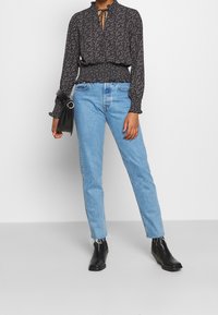 Blusa nera floreale con collo alto e dettaglio a fiocco, abbinata a jeans azzurri a gamba dritta e stivali neri alla caviglia. Borsa a mano semplice.