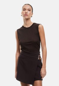 Top marrón sin mangas combinado con una falda envolvente negra de cintura alta con un acento dorado. Tela suave con un diseño ajustado.