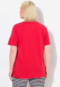 Chemise rouge à manches courtes avec un col rond, fabriquée en tissu doux. Portée avec un pantalon à rayures noir et blanc arborant un motif de cerises.