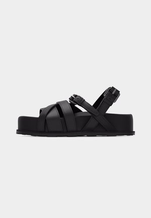 Black platform sandal with crisscross leather straps and adjustable ankle buckle.