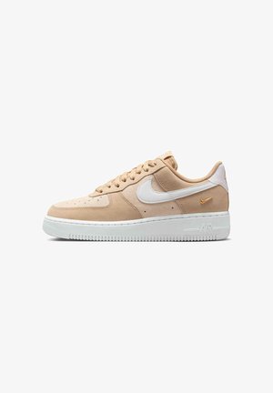 Beige suède Nike Air Force 1 sneaker met wit swoosh-logo, witte zool, beige veters en een kleine oranje geborduurde swoosh bij de hiel.