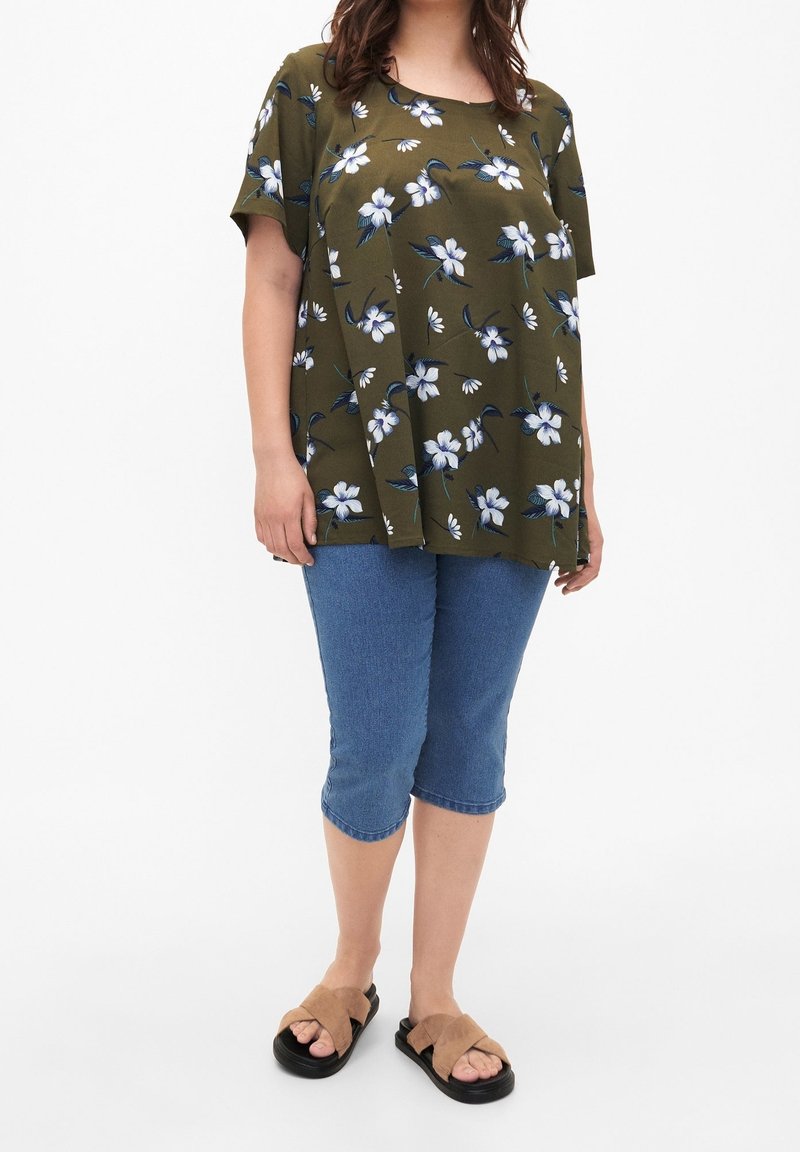 Top floral verde oliva con mangas cortas, combinado con jeans capri azul claro. Sandalias color canela con diseño cruzado. Ajuste simple y relajado.