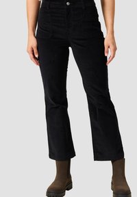 Pantalones de pana negros acampanados con bolsillos frontales, cierre de botón y una textura suave. Combinados con botas cortas marrones.