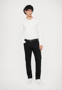 Λευκή μακρυμάνικη μπλούζα με V-λαιμό, μαύρο παντελόνι, μαύρη ζώνη και λευκά αθλητικά παπούτσια. Απλός σχεδιασμός με εφαρμοστή σιλουέτα.