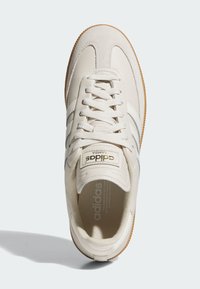 Sneakers Adidas Samba w kremowej skórze z szarymi paskami, z teksturowanym noskiem, płaskimi sznurowadłami i gumową podeszwą. Złoty akcent z logo.