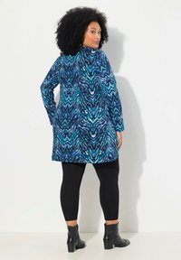 Tunic a maniche lunghe in blu e nero con motivo astratto, realizzata in tessuto morbido, abbinata a leggings neri e stivaletti alla caviglia.