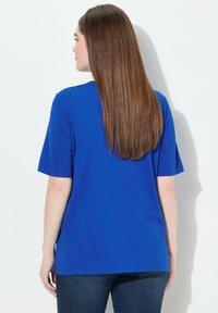 Modré bavlněné tričko s krátkými rukávy, rovný lem a kulatým výstřihem. Pohled zpočátku ukazuje hladkou, lehkou látku a uvolněný střih.
