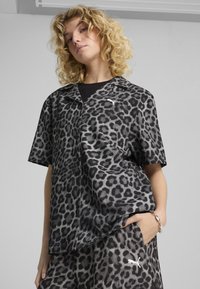 Camicia a maniche corte in tessuto con stampa leopardata nera e grigia. Presenta un colletto, chiusura frontale con bottoni e un discreto dettaglio del logo.