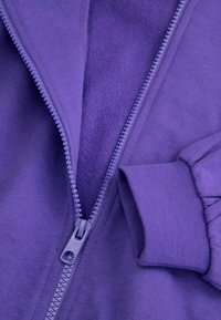 Fioletowa bluza z zamkiem błyskawicznym, z miękkim wnętrzem typu terry, ściągaczami przy mankietach i gładką powierzchnią na zewnątrz, z zamkiem w dopasowanym kolorze.