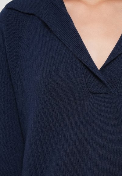 Laivastonsininen neulepusero, jossa on V-kaula-aukko ja suuri kaulus. Ominaisuuksiin kuuluu ribbikuviointi ja rento istuvuus.