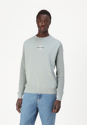 Felpa a maglia verde chiaro con polsini e orlo a costine, con logo centrale "Calvin Klein Jeans" in nero. Abbinata a jeans blu.