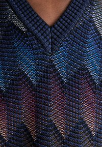 Pletený sveter s výstrihom do V v tmavomodrej farbe so vzorom chevron v odtieňoch modrej, fialovej a červenej. Štruktúrovaná tkanina s rebrovanými okrajmi.