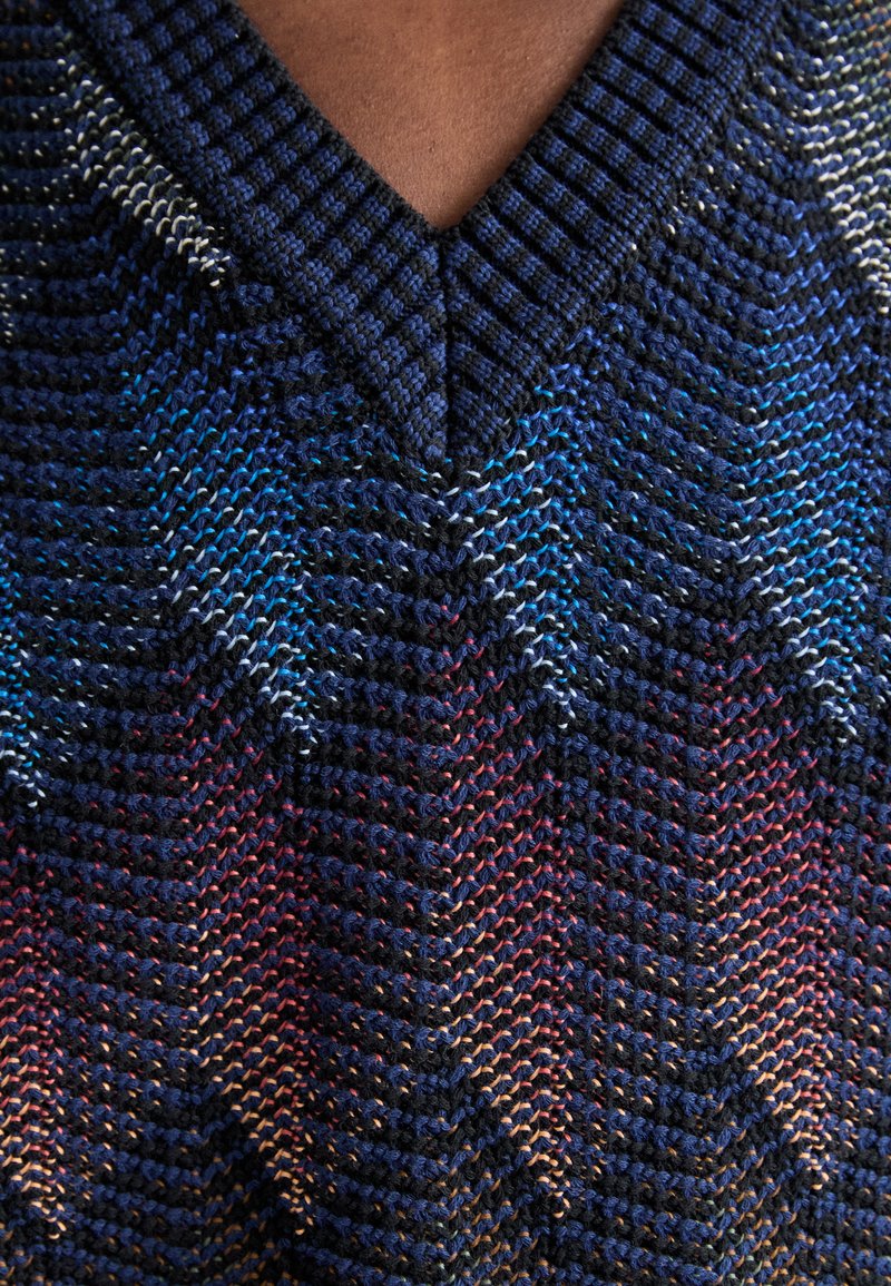 Maglione a V in blu scuro lavorato a maglia con un motivo a chevron che presenta tonalità di blu, viola e rosso. Tessuto testurizzato con bordi a coste.