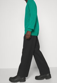 Grön stickad tröja med ribbad mudd och nederkant, ihopparad med vida svarta byxor och svarta slip-on skor med en kraftig sula.