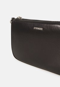 Borsa clutch nera in pelle con una texture liscia, dotata di una zip argentata e di un piccolo dettaglio logo argentato. Forma rettangolare, design minimalista.