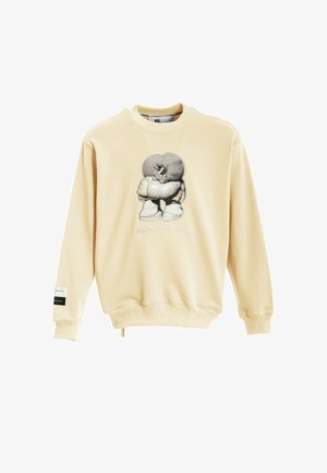 Sudadera beige con cuello redondo, que presenta un gráfico impreso de un personaje en el frente y una etiqueta de logo en la manga.