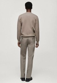 Light brown, textured sweater with a round neckline, paired with light gray tailored trousers. Black shoes complete the look.