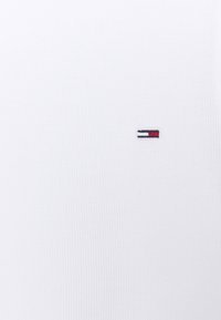 T-shirt bianco in cotone con texture a coste, dotato di un piccolo logo rettangolare ricamato in rosso, bianco e navy.