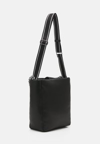 Sac à épaule rembourré noir de forme carrée, avec une bandoulière réglable rayée et des accents en matériel argenté.