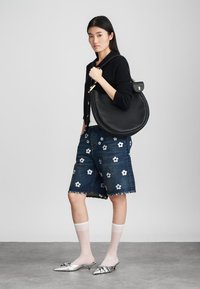 Sac en cuir noir en forme arrondie avec des accessoires en or, porté sur un cardigan noir, associé à un short en denim à motifs floraux.
