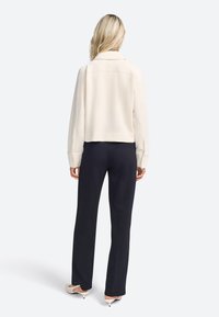 Crème-kleurig, cropped jack met een omgevouwen kraag en lange mouwen, gecombineerd met donkere broek en lichtgekleurde hakken. Gladde, zachte textuur.