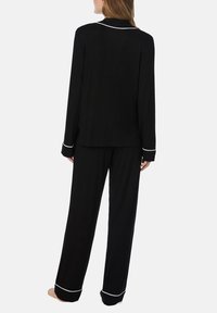 Ensemble de pyjama noir comprenant un haut à manches longues avec une bordure blanche et un pantalon assorti. Le tissu a une texture lisse et une coupe ample.