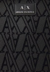 Melna struktūrēta virsma ar izcilu "AX" logo rakstu un taisnstūra etiķeti, kurā baltā krāsā ir redzams ieraksts "A|X ARMANI EXCHANGE".