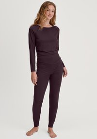 Langsleeve top en strakke broekset in diep paarse stof. Soepele textuur, ribbels aan de manchetten en een hoge tailleband voor een goede pasvorm.