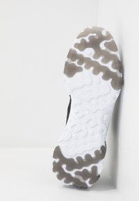 Zwarte sneakerzool met een getextureerde witte rubberen bovenlaag en grijze accenten. Heeft golvende patronen en een gebogen vorm voor grip en flexibiliteit.