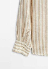 Poignet de chemise à manches longues avec des rayures verticales beige et blanc et un seul bouton sur le poignet sur un fond blanc.