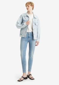 Világoskék farmerdzseki fehér felsőn, világoskék skinny farmerral és fekete magassarkú szandállal párosítva. Egyszerű dizájn klasszikus fém kiegészítőkkel.