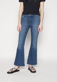 Siniset liehukkeet farkut, joissa on keskikorkea vyötärö ja pehmeä denim-kangas. Niissä on klassinen viiden taskun malli ja hienovarainen haalistuma reisissä.