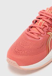Rosa Sportschuh mit einem strukturierten Mesh-Obermaterial, kontrastierender weißer Sohle und einem auffälligen Schnürsystem. Mit einem goldenen Akzentlogo an der Seite.