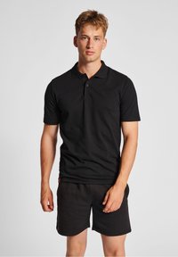 Black polo shirt with a classic collar, short sleeves, two-button placket, and a textured fabric. Paired with black shorts featuring a small logo.