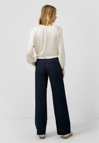 Kremowa bluzka z odkrytymi ramionami i bufkami w połączeniu z ciemnoniebieskimi spodniami o szerokich nogawkach. Obuwie z srebrnym akcentem, który dodaje kontrastu.