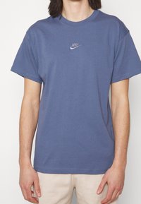Camiseta de algodón azul con mangas cortas, cuello redondo y un pequeño logo blanco de Nike en el pecho. Textura suave y corte relajado.