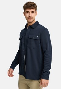 Chemise boutonnée bleu marine en tissu texturé, dotée de deux poches poitrine, de manches longues et d'un col.