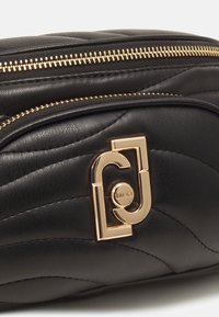 Zwarte leren tas met een gequilt ontwerp, voorzien van een gouden ritssluiting en een gouden logo-sluiting. Gladde textuur met zichtbare stikselaccenten.