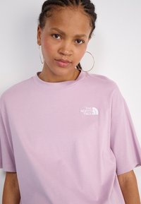 Helles rosa, übergroßes T-Shirt aus Baumwolle mit kurzen Ärmeln und Rundhalsausschnitt. Mit einem weißen Logo auf der linken Brust.