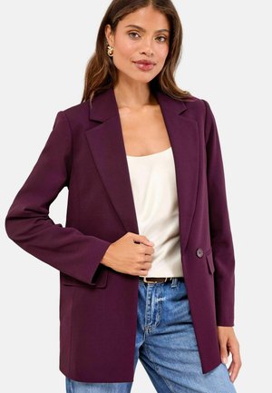 Purple blazer with a structured design, single button closure, and two front pockets, paired with a cream top and blue jeans. Silk-like texture.