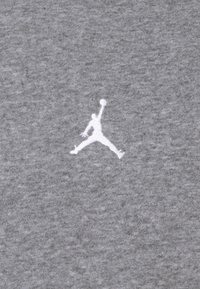 Tessuto di cotone grigio caratterizzato da un logo Jumpman ricamato in bianco. La texture risulta morbida e leggermente melangiata. Design semplice e minimale.