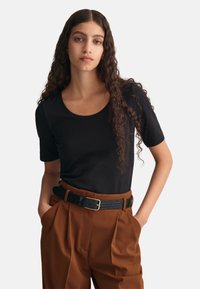 Sort kortærmet skjorte med rund halsudskæring, båret med højttaljede brune bukser og et struktureret sort bælte med en guldbuckle.