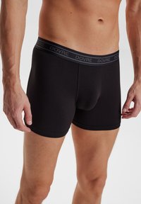 Sorte boxer briefs lavet af blødt, strækbart materiale, med en grå elastik i taljen med "DOVRE" branding. Tæt design og glat tekstur.