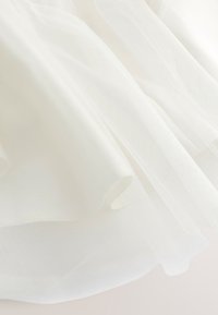 Tessuto bianco leggero e trasparente con pieghe morbide e una texture delicata e traslucida.